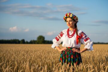 Młoda kobieta w tradycyjnym stroju ludowym stoi na polu pszenicy podczas dożynek.