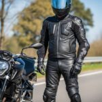 Motocyklista w pełnym sprzęcie ochronnym stoi przy nowoczesnym motocyklu na otwartej drodze.