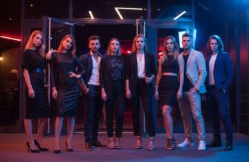 Grupa młodych osób w modnych strojach stoi przed klubem nocnym przy kolorowych neonach.