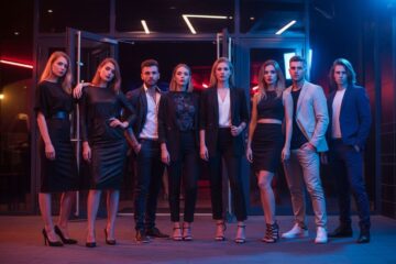 Grupa młodych osób w modnych strojach stoi przed klubem nocnym przy kolorowych neonach.