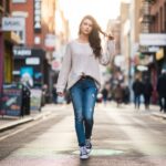 Młoda kobieta w jeansach i sneakersach pewnie spaceruje ulicą w miejskim otoczeniu przy naturalnym świetle