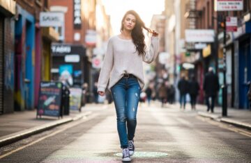 Młoda kobieta w jeansach i sneakersach pewnie spaceruje ulicą w miejskim otoczeniu przy naturalnym świetle