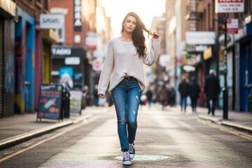 Młoda kobieta w jeansach i sneakersach pewnie spaceruje ulicą w miejskim otoczeniu przy naturalnym świetle